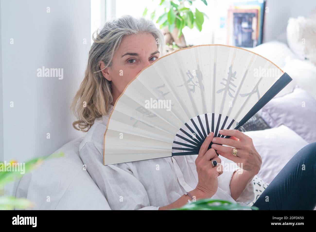 Ältere Frau kühlt ihr Gesicht mit einem Ventilator. Stockfoto