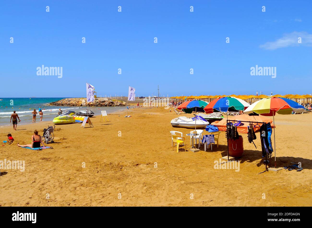 Touristen, die sich am Strand von Gouves auf der Insel Kretas, der größten und bevölkerungsreichsten der griechischen Inseln, sonnen Stockfoto