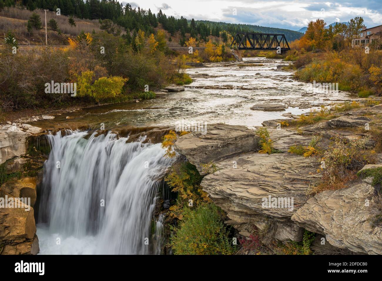 Lundbreck Falls, ein Wasserfall des Crowsnest River in Herbstlaub Saison. Eine Eisenbrücke für Eisenbahnschienen im Hintergrund. Alberta, Kanada. Stockfoto