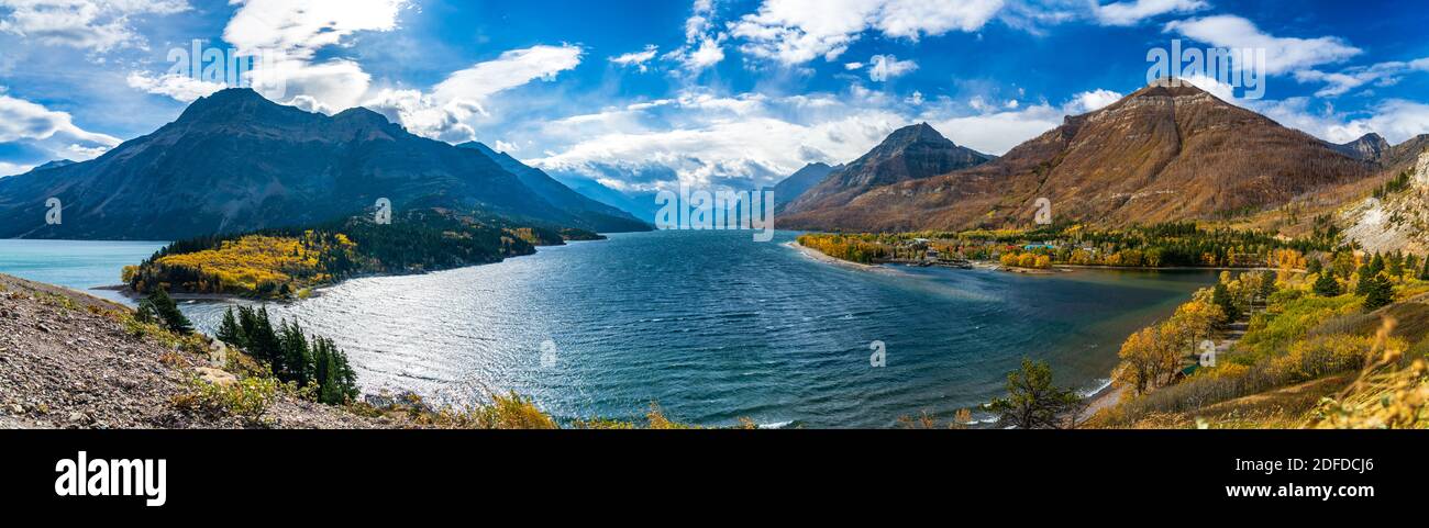 Upper Waterton Lake Seeufer im Herbst Laubsaison sonniger Tag Morgen. Blauer Himmel, weiße Wolken über Bergen im Hintergrund. Wahrzeichen Stockfoto