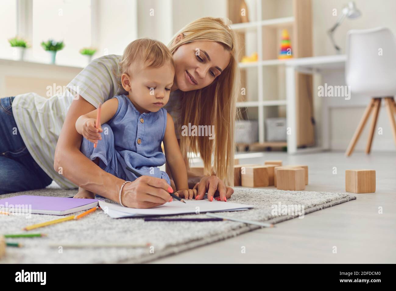 Junge Kindermädchen Lehre liebenswert Kleinkind zu zeichnen mit Bleistiften sitzen Auf dem Boden im Spielzimmer Stockfoto