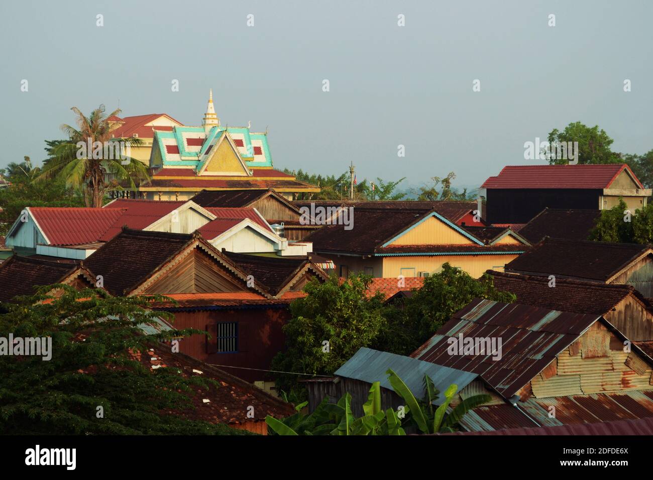 Stadtbild von Hausdächern und Wat (buddhistischer Tempel) auf einem Hintergrund. Tropische Landschaft mit Palmen. Stung Treng, Kambodscha Stockfoto