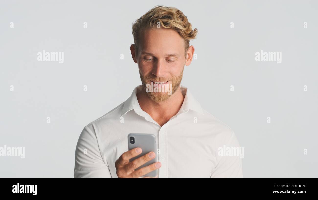 Schöner bärtiger Mann im Hemd selbstbewusst mit Smartphone für die Arbeit über weißem Hintergrund. Junger Geschäftsmann, der am Telefon arbeitet Stockfoto