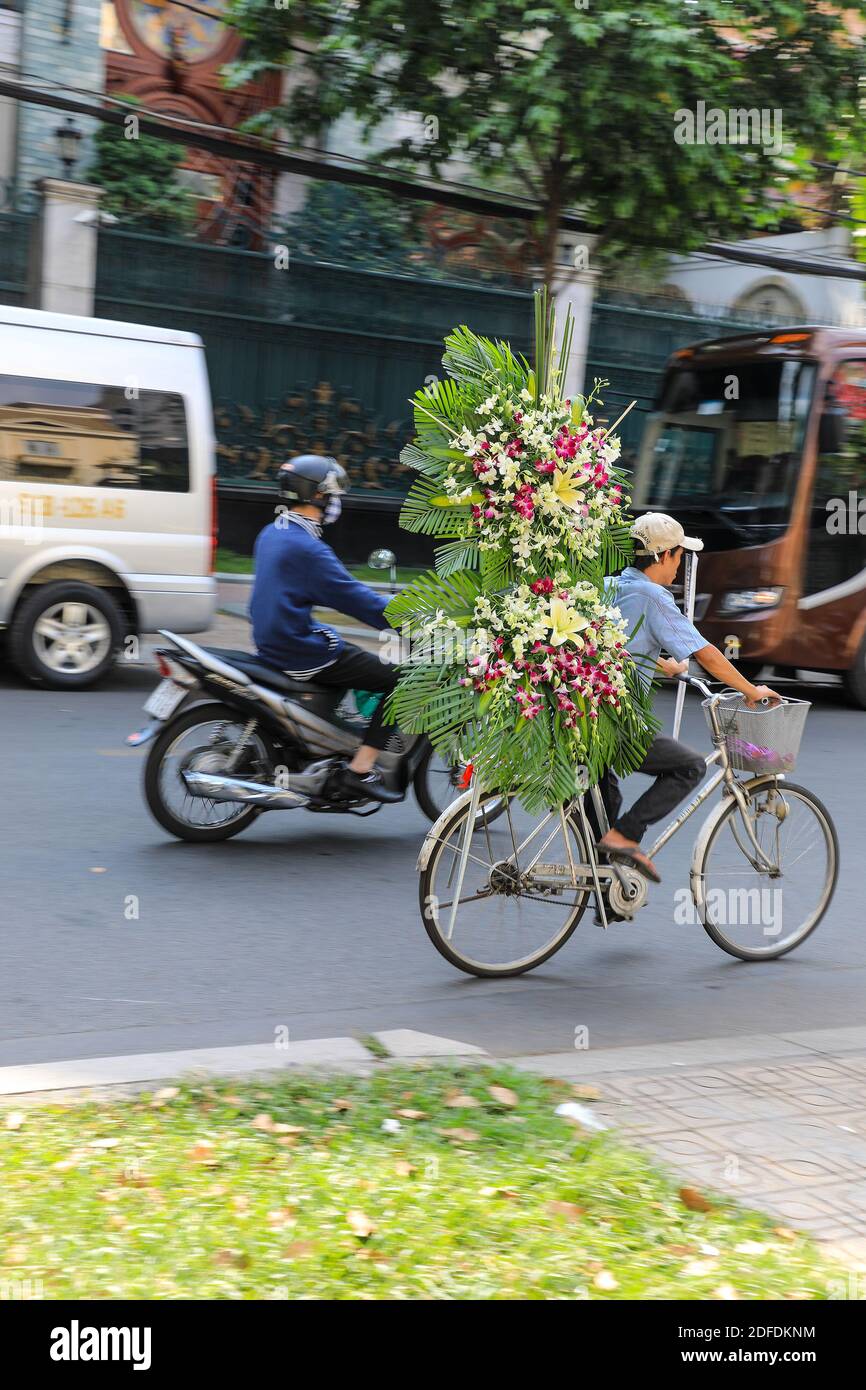 Ein Mann, der auf der Straße ein Fahrrad fährt und eine sehr große Blumenpracht trägt, Ho Chi Minh City, Vietnam, Asien Stockfoto