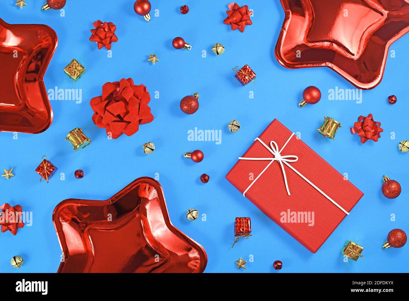 Weihnachten flach Lay mit roten Stern geformten Papier Party Teller, Baum Kugel Ornamente, Geschenkbox und Geschenkbänder, Sterne und Glocken auf blauem Hintergrund Stockfoto
