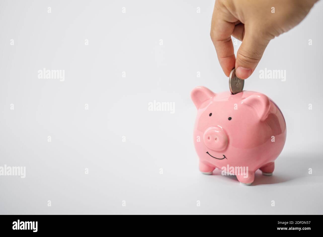 Nahaufnahme der Hand Putting Coin Into Piggy Bank. Sparkonzept. Stockfoto