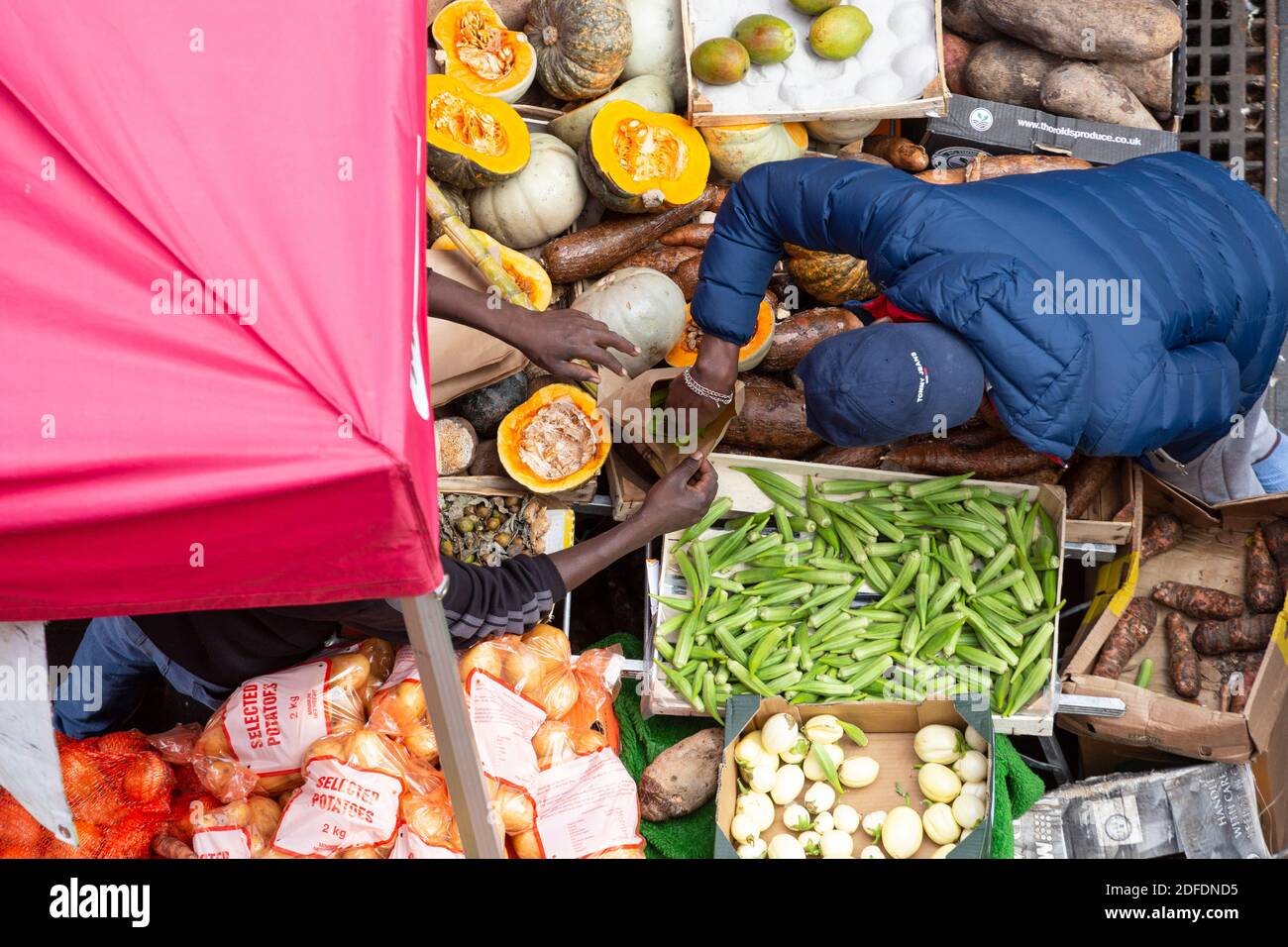 Blick von oben auf Leute, die Gemüse in eine Tasche stecken, an einem Straßenstand in Brixton Market, Electric Avenue, Brixton, London Stockfoto