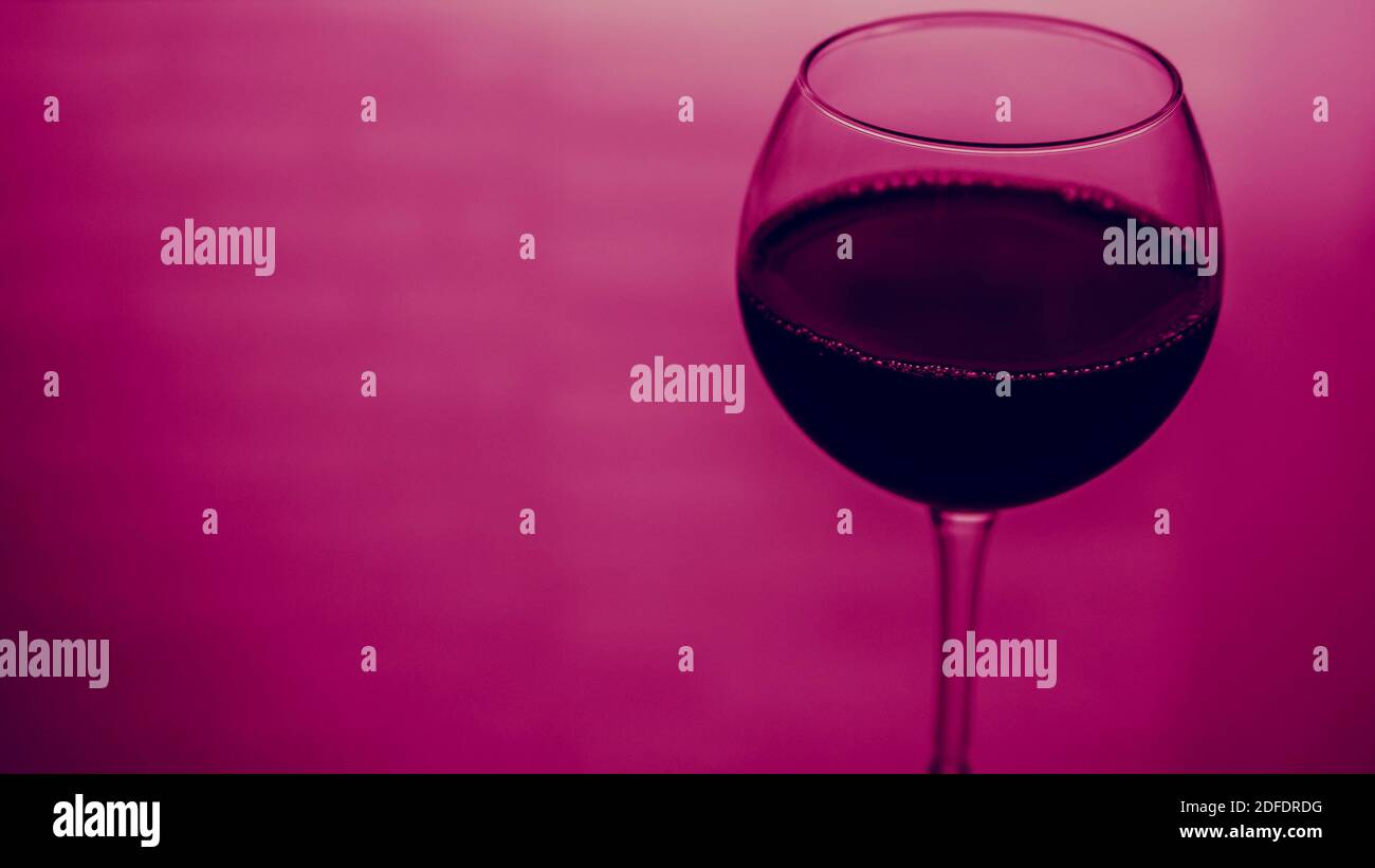 Glas Rotwein Platz für Text, Rotwein in einem Glas auf einem bunten rosa Hintergrund. Stockfoto