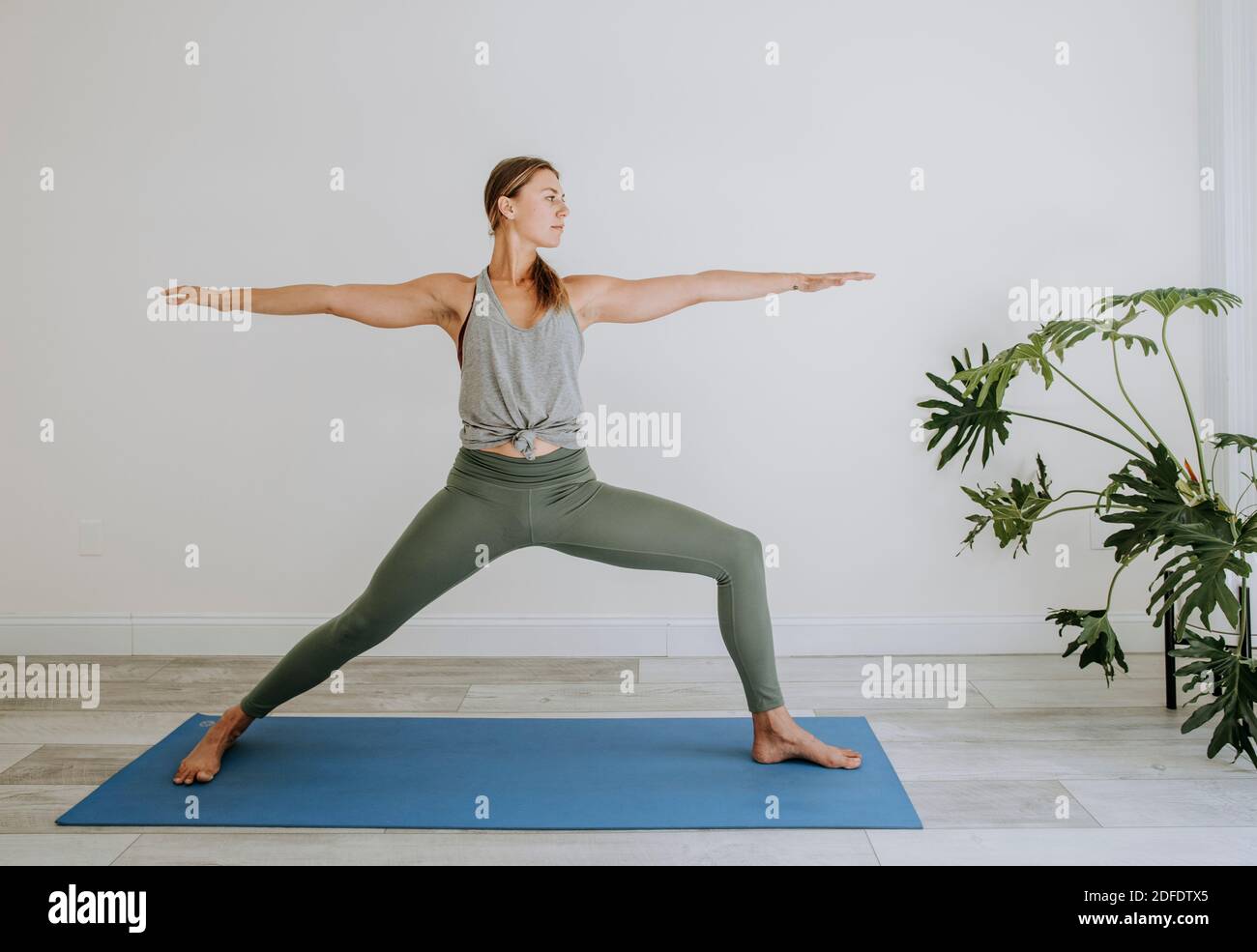 Athletische Frau tut Krieger Yoga Pose drinnen auf blauer Matte Stockfoto