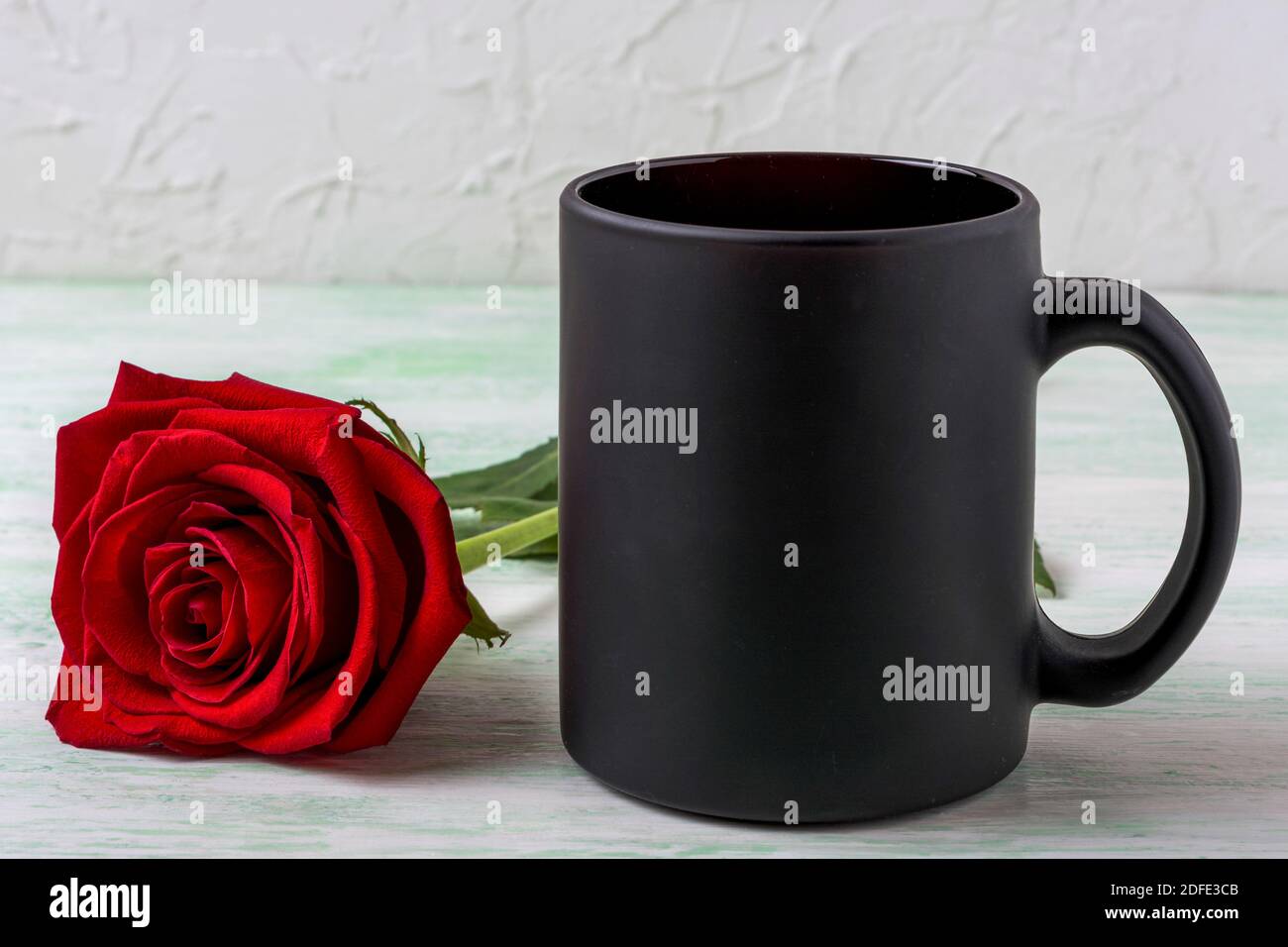 Schwarzer Kaffeebecher Mockup mit schöner roter Rose. Leerer Becher für Markenwerbung. Stockfoto