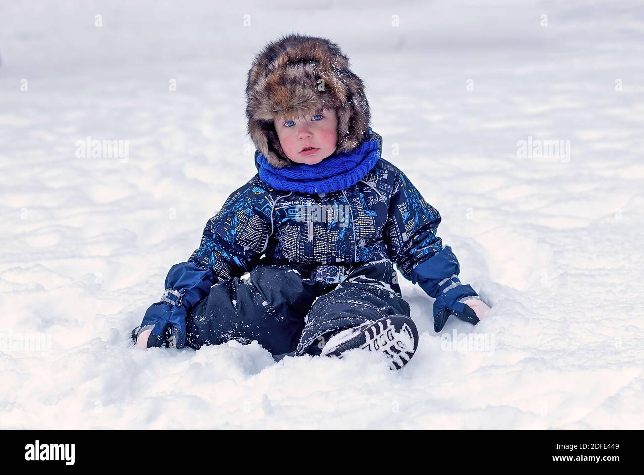 Lustige kleine Junge in Overalls und Pelz Hut Kleidung spielen im Freien während Schneefall. Aktive Erholung mit Kindern im Winter an kalten verschneiten Tagen. Frohes Kind Stockfoto