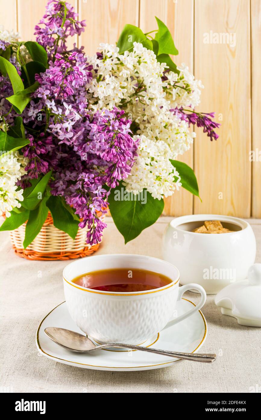 Tasse Tee und Zweig der Fliederblume auf Leinentischdecke. Frühlings-Tee-Zeit-Konzept. Frühstückstee Tasse. Stockfoto