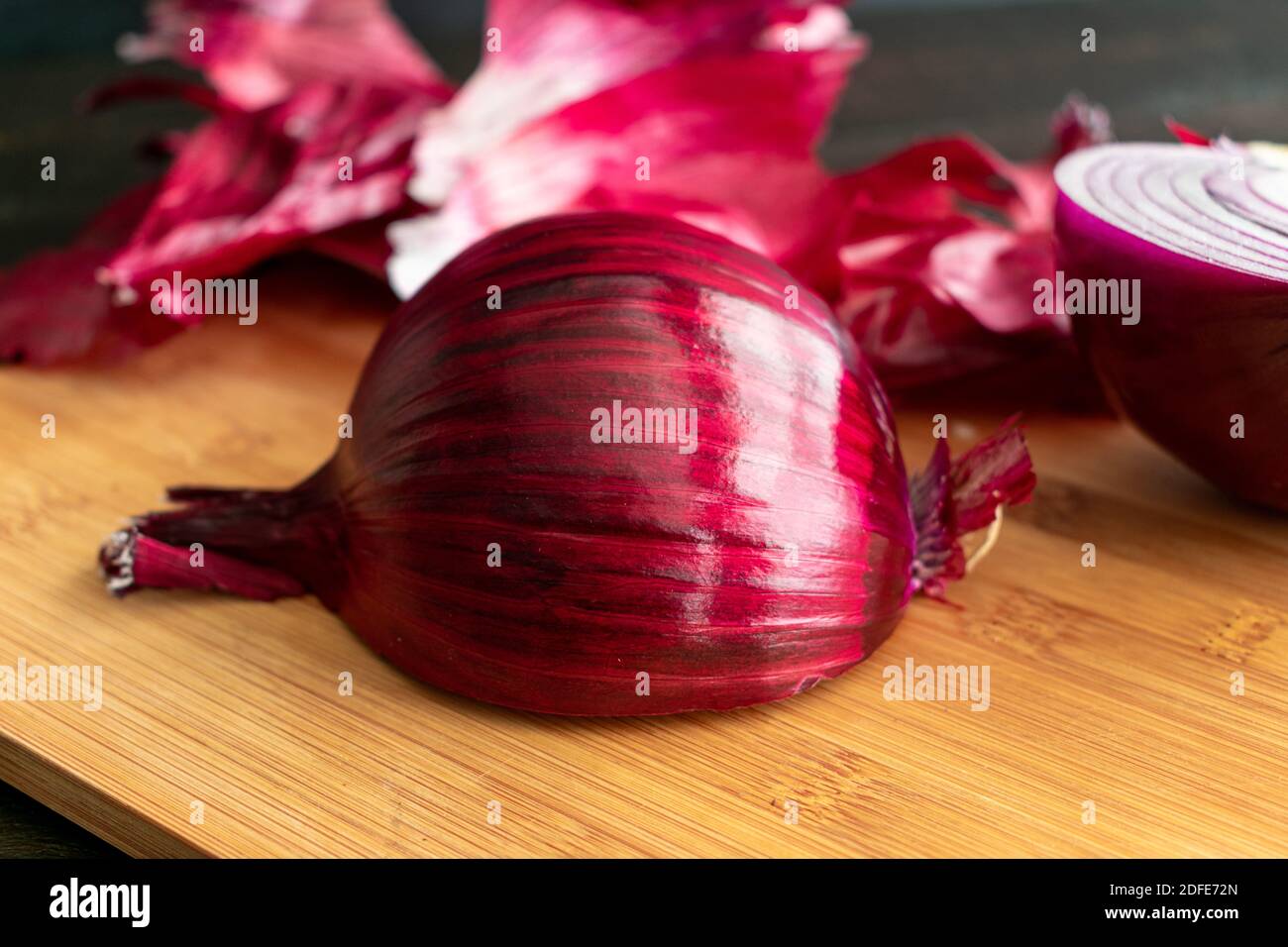 Schneiden einer roten Zwiebel: Schälen und Schneiden einer spanischen Zwiebel auf einem Bambus Schneidebrett Stockfoto