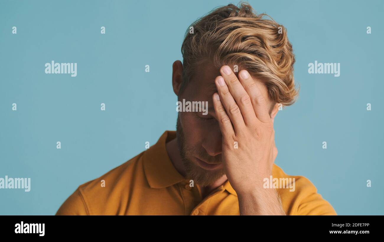 Junger bärtiger Mann sieht müde posiert vor der Kamera über bunten Hintergrund. Verärgerter Mann Stockfoto
