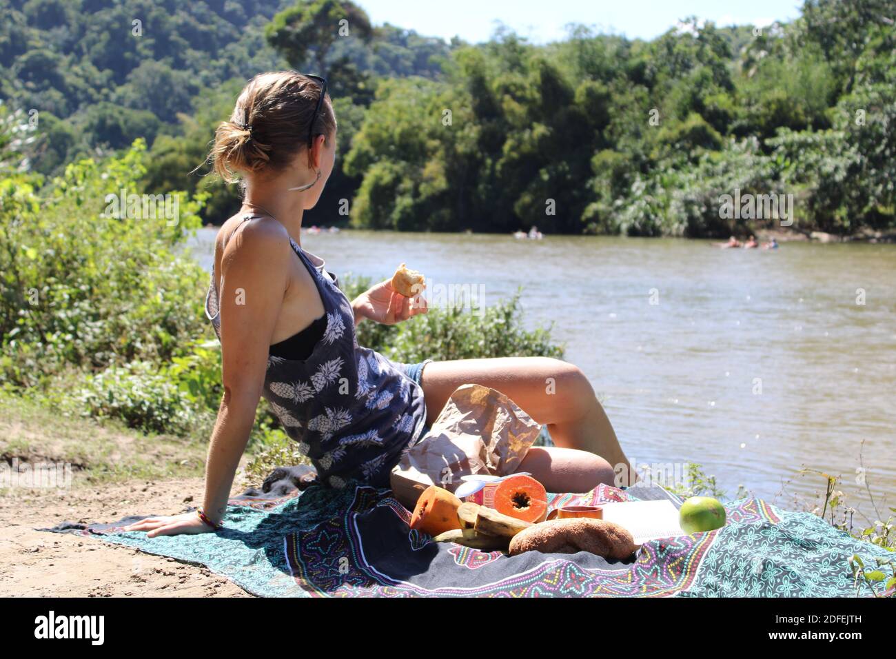 Eine Frau genießt ihr Picknick, während sie den Fluss betrachtet. Stockfoto