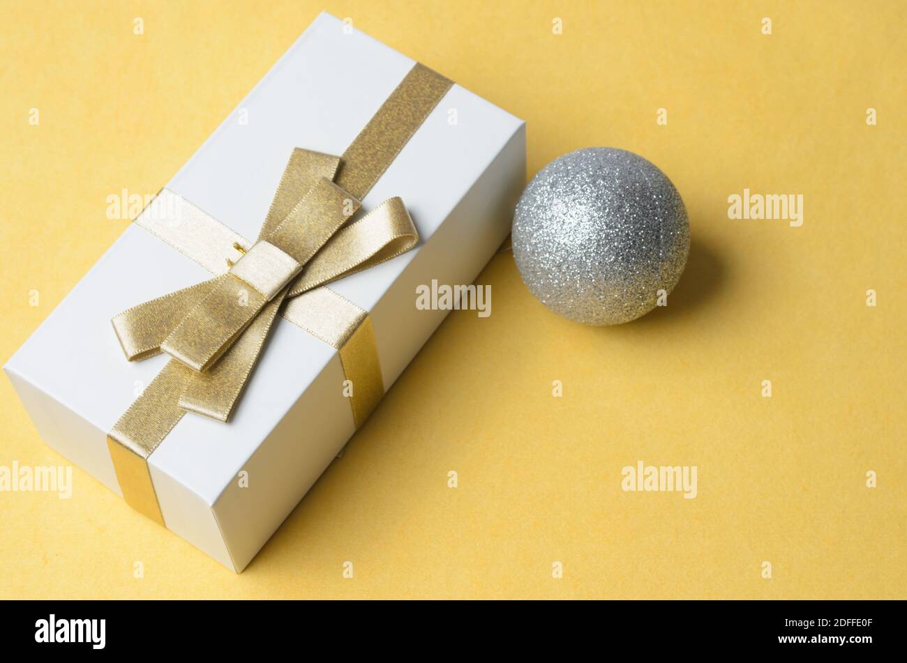 Geschenkbox mit goldenem Band mit Weihnachtsdekorationen auf gelbem strukturiertem Hintergrund gebunden. Selektiver Fokus. Stockfoto