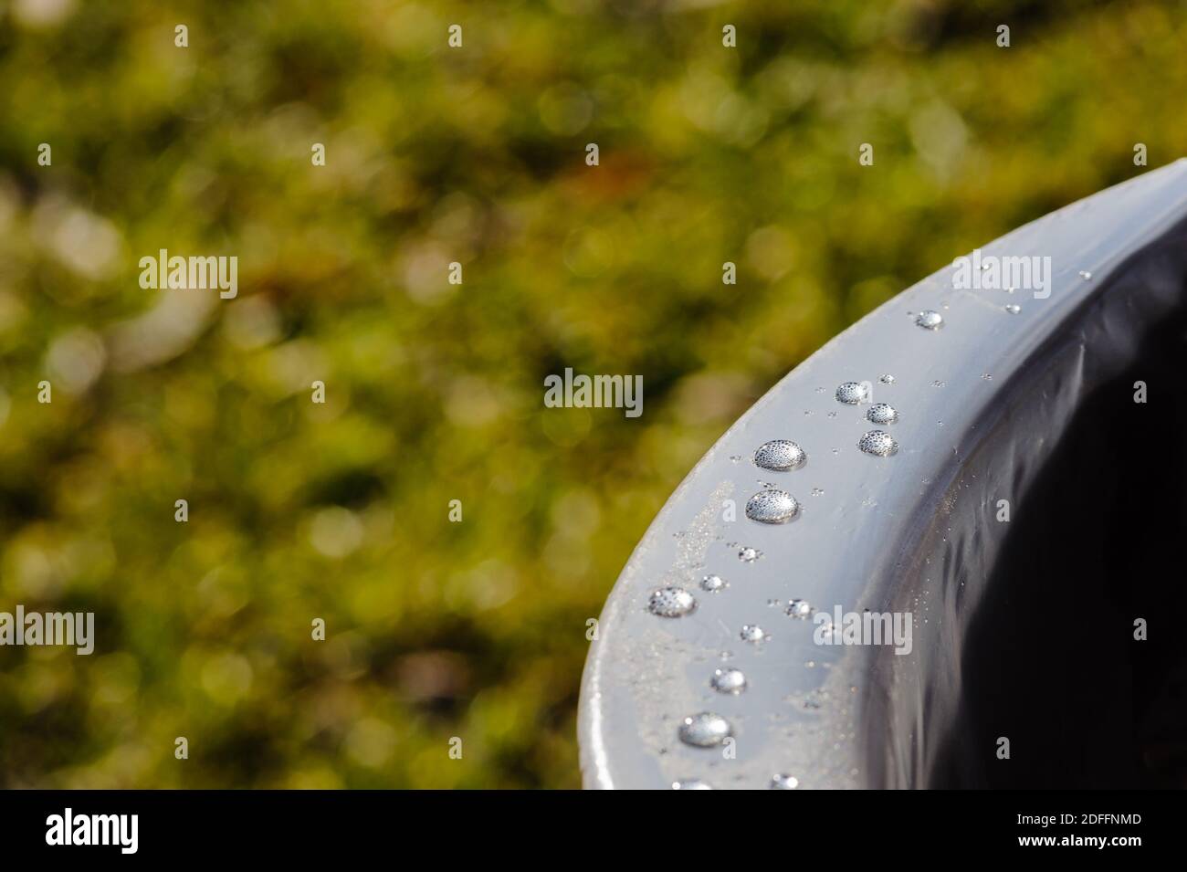 Nahaufnahme von Wassertropfen auf glatter Metalloberfläche vor verschwommenem grünen Hintergrund. Stockfoto