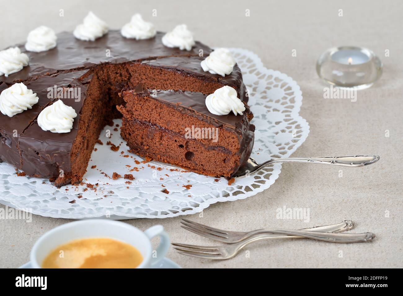 Köstliche Wiener Kakaokuchen mit roter Johannisbeermarmelade und bedeckt mit feiner dunkler Schokolade und Sahne, serviert mit Kaffee Stockfoto
