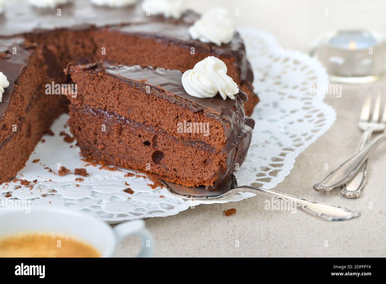 Köstliche Wiener Kakaokuchen mit roter Johannisbeermarmelade und bedeckt mit feiner dunkler Schokolade und Sahne, serviert mit Kaffee Stockfoto