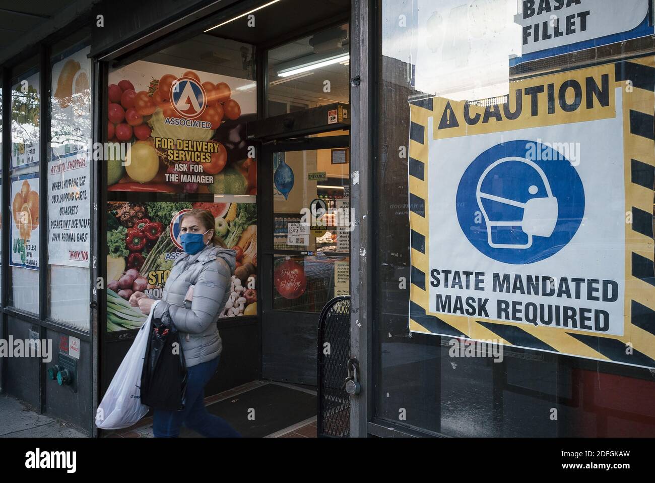 Queens, New York. 03. Dezember 2020.EINE Frau verlässt einen Supermarkt mit einem Schild mit der Aufschrift "Mandat des Zustands Maske erforderlich" Stockfoto