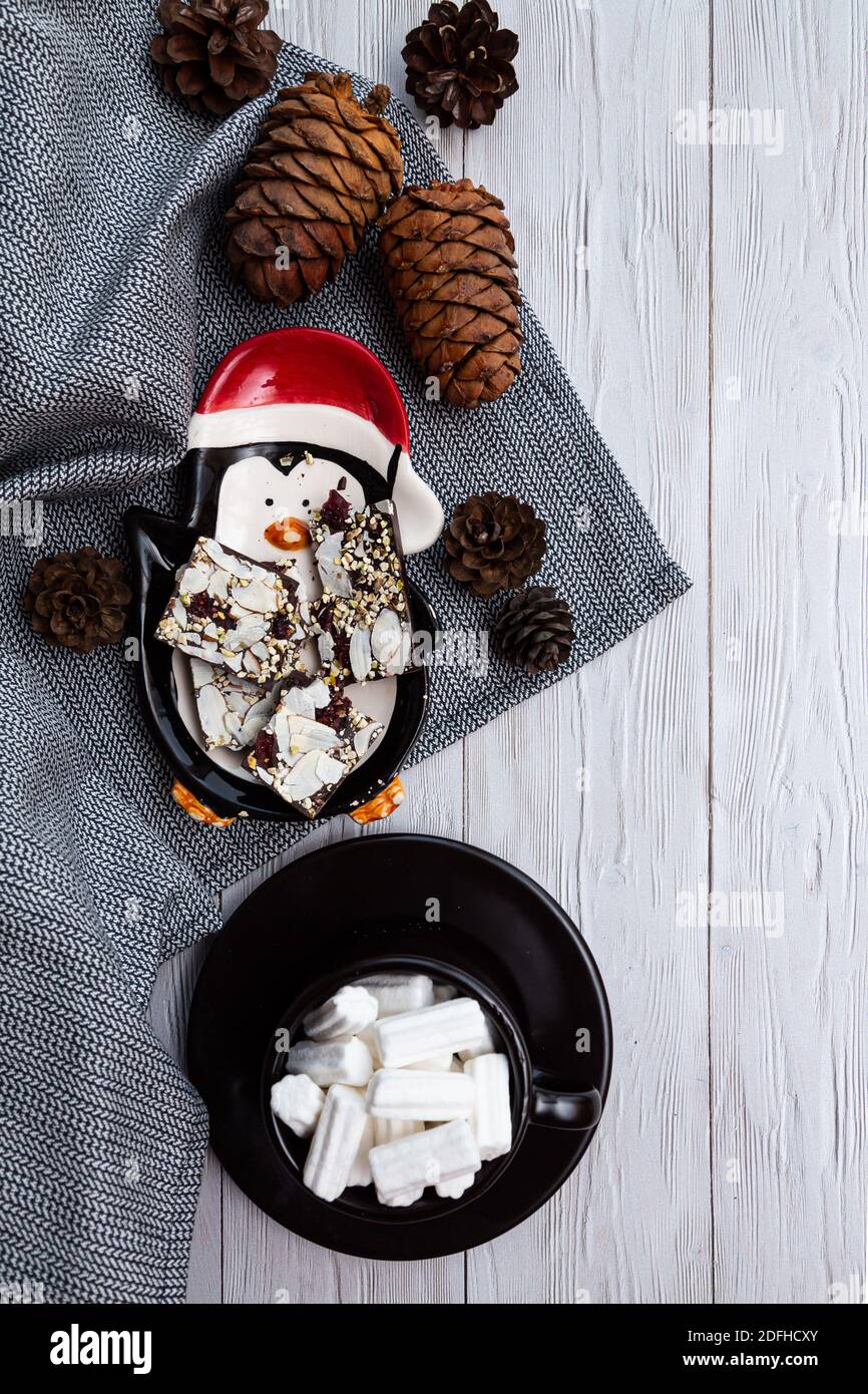 Gemütliches, winterliches, minimalistisches Stillleben mit Zedernkegel, Schokolade und einer Tasse Marshmallows auf einem hellen Holztisch Stockfoto