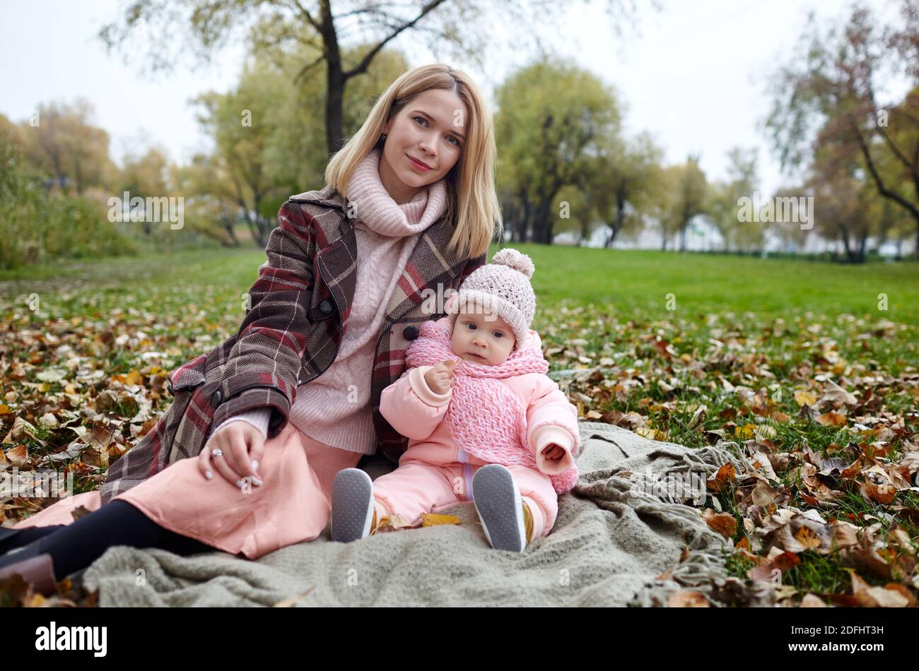 Schöne Baby-Mädchen mit Mutter auf dem Plaid sitzen. Familien im Freien. Liebenswert kleines Mädchen in warmen Kleidern bei Picknick im Herbst Park an sonnigen Tag. Stockfoto
