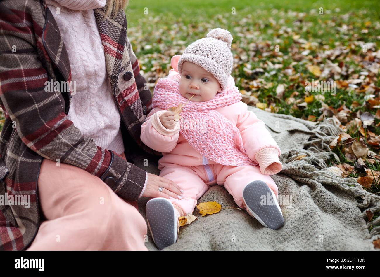 Schöne Baby-Mädchen mit Mutter auf dem Plaid sitzen. Familien im Freien. Liebenswert kleines Mädchen in warmen Kleidern bei Picknick im Herbst Park an sonnigen Tag. Stockfoto