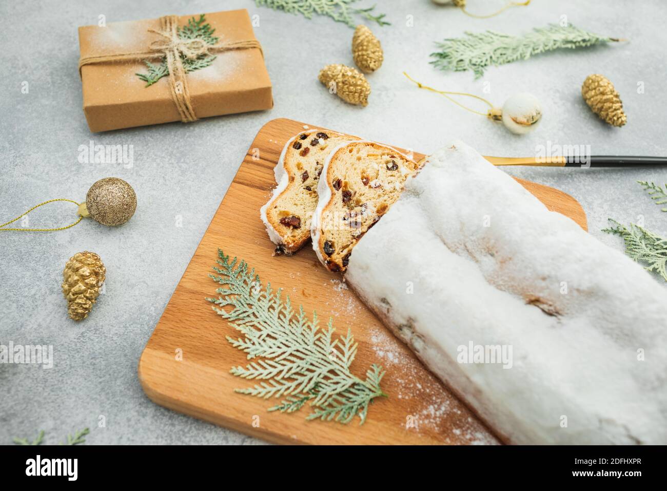 Weihnachtskomposition mit Stollenkuchen auf Holzbrett, Besteck und Geschenk auf grauem Hintergrund Stockfoto
