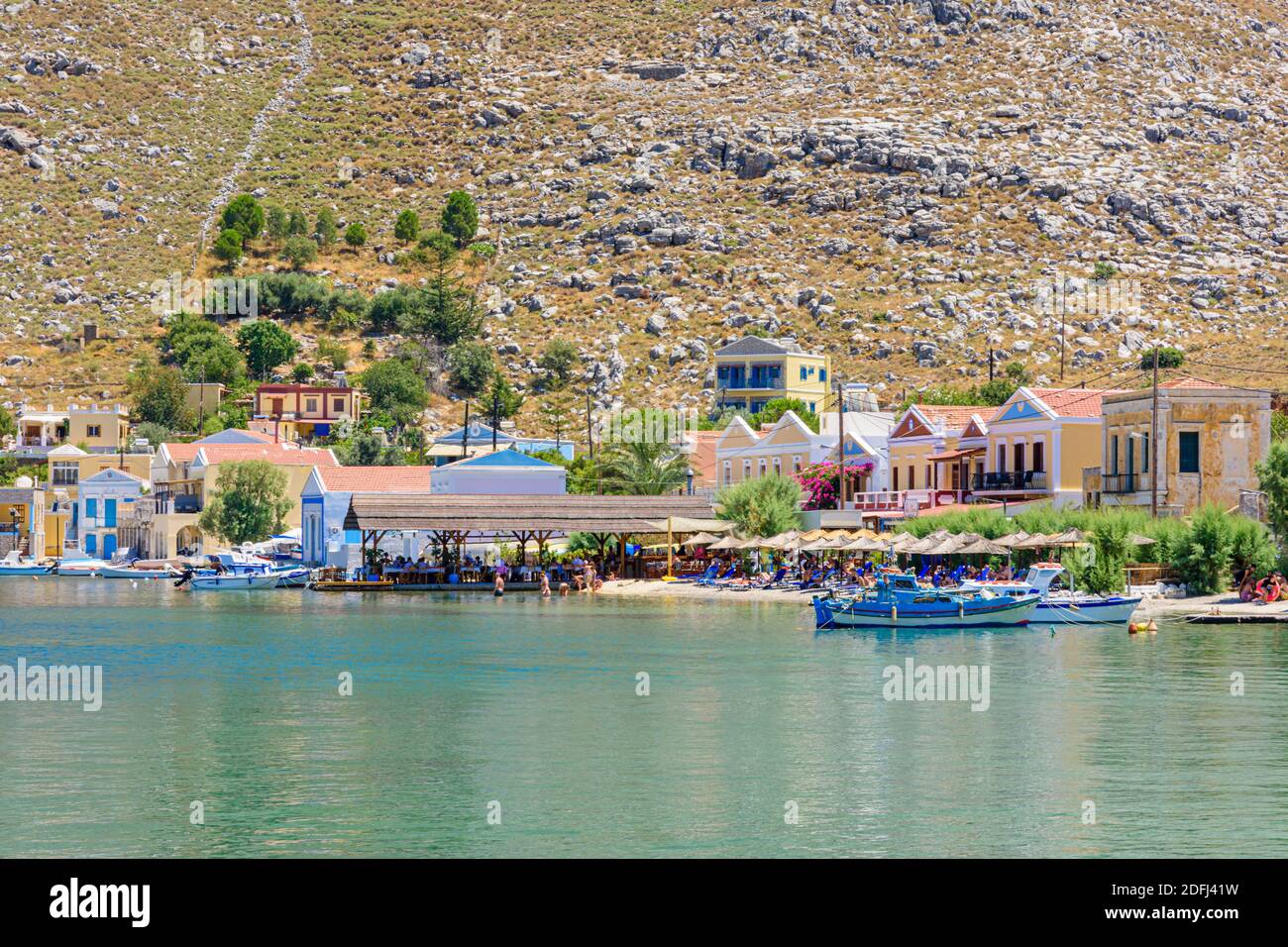 Taverne am Wasser und Sonnenschirme in Pedi Bay, Symi Island, Dodekanes, Griechenland Stockfoto