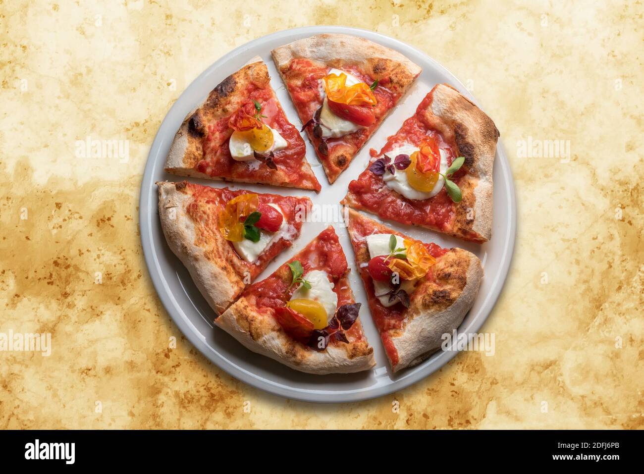 Gourmet-Pizza mit Tomate, Mozzarella, Basilikum und knuspriger Pfefferhaut. Sechs Scheiben in weißer Platte in der Draufsicht auf gelbem Marmor Hintergrund Stockfoto