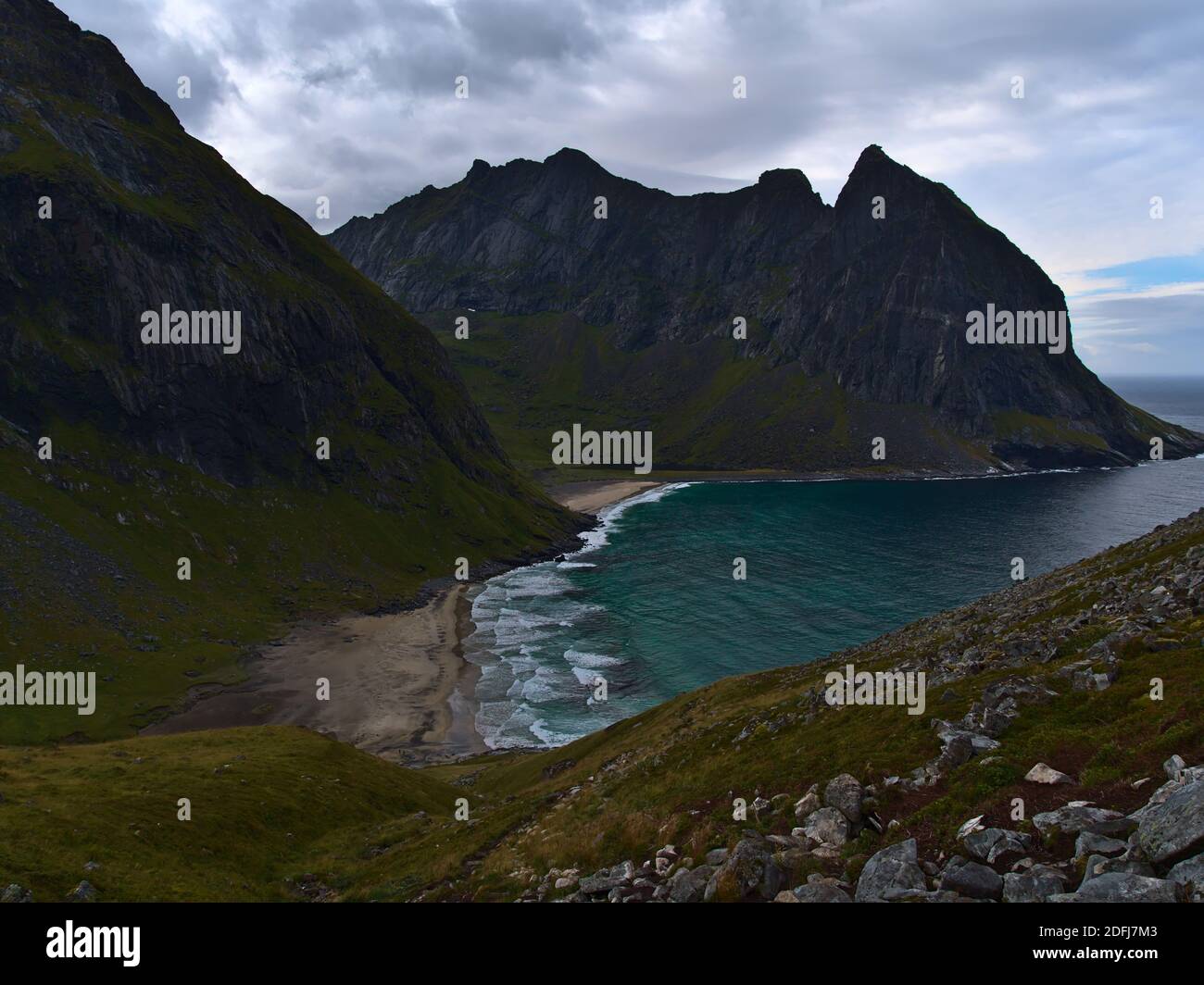 Atemberaubender Blick auf den Kvalvika Beach mit wilder Brandung, umgeben von steilen, zerklüfteten Bergen und felsigen Wiesen an bewölkten Tagen im Spätsommer in Norwegen. Stockfoto