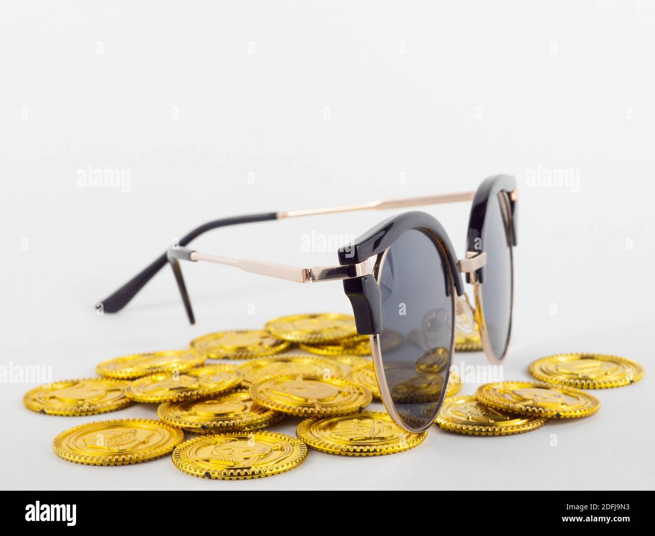 Eine Sonnenbrille auf einem Haufen Goldmünzen. Konzept für Geld und Urlaub. Stockfoto