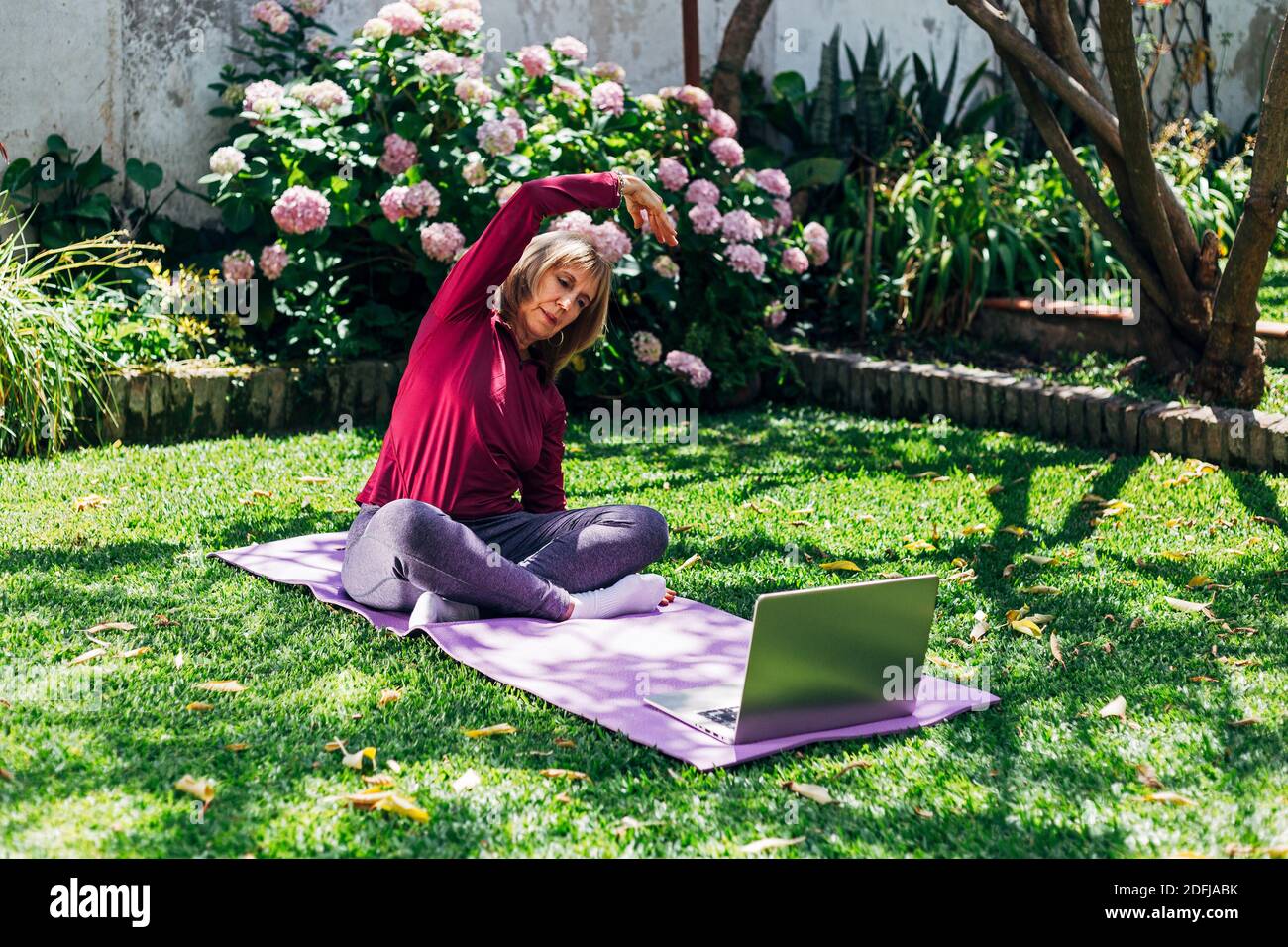 Online Sport Fitness Yoga Training Workout, Senior Frau im Garten ihres Hauses macht Übungen auf Pilates Matte gegenüber Laptop zu Hause. Stockfoto