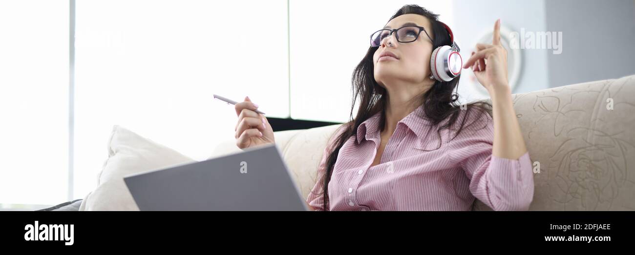 Frau mit Kopfhörer sitzen auf der Couch, hören Audio und merken sich Text. Stockfoto