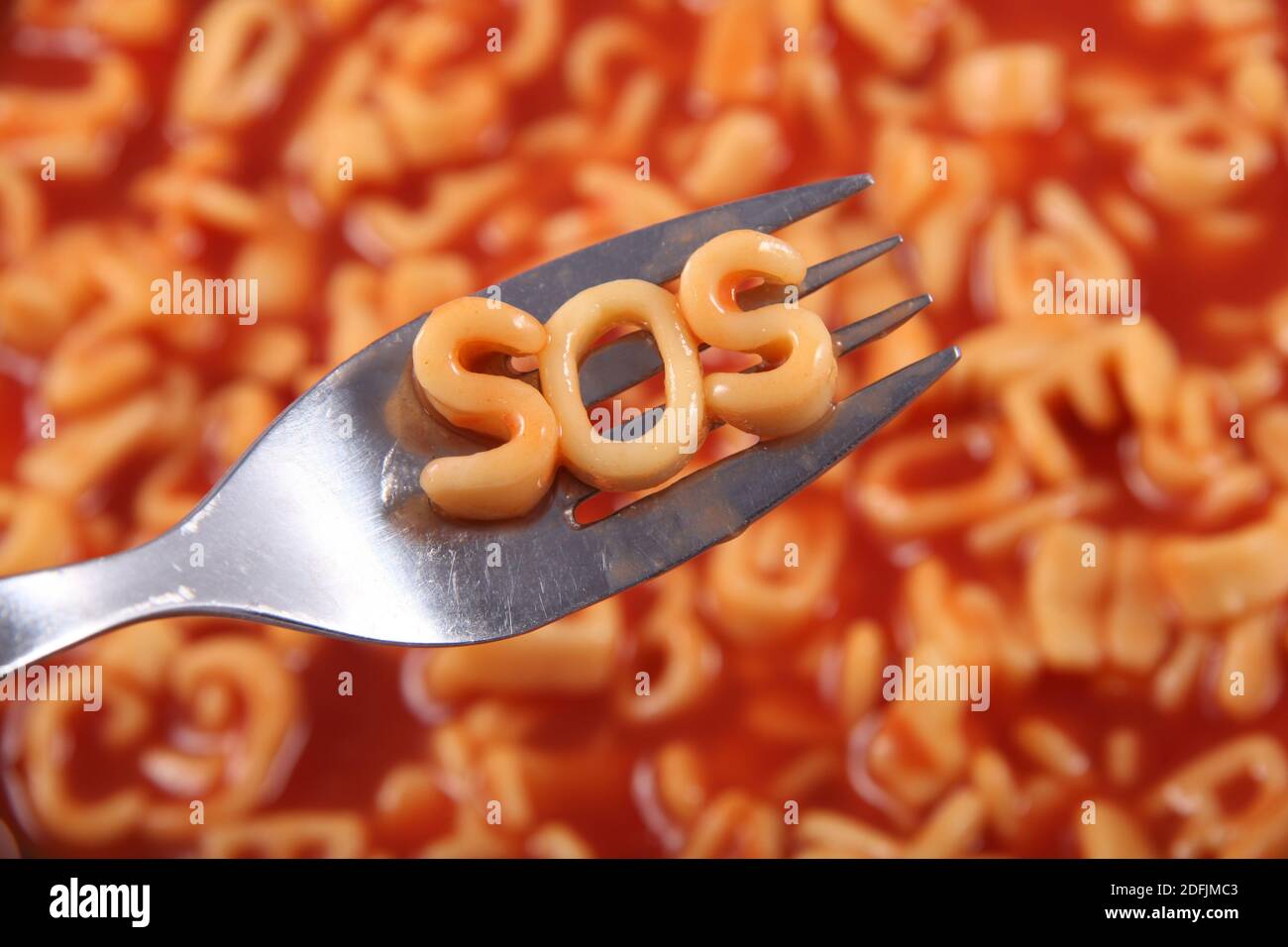 Spaghetti-Buchstaben Schreibweise das Wort SOS steht für Save our Souls, mit den Buchstaben auf einer Gabel gehalten, dahinter ist die rote Tomatensauce. Stockfoto