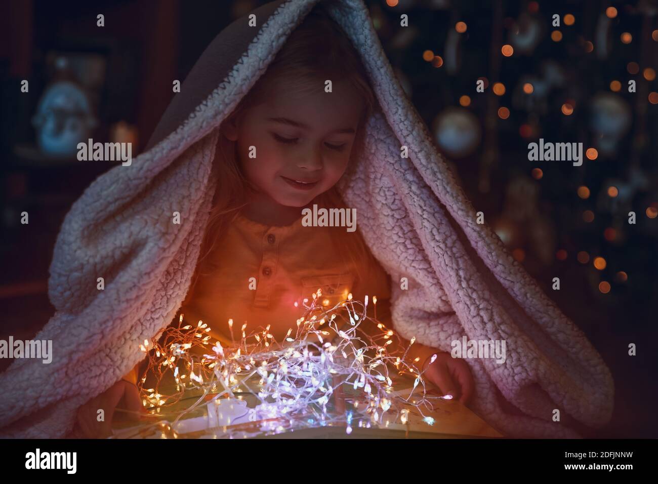 Porträt eines niedlichen kleinen Babys mit einer Decke bedeckt. Genießen Sie magische Lichter der Weihnachtsbaum Dekoration. Frohe Winterferien zu Hause. Stockfoto