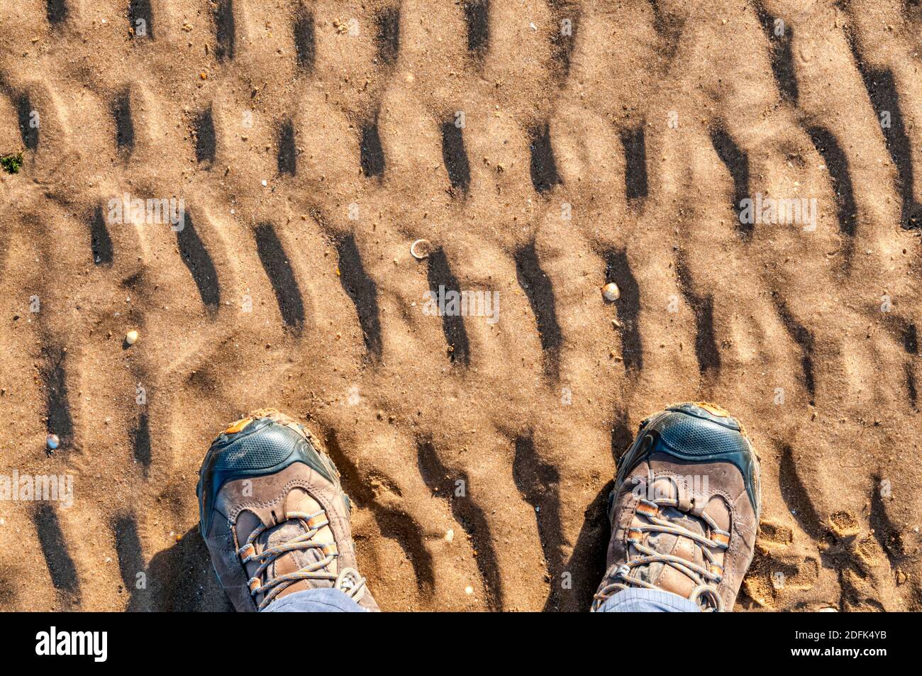 Ein Paar Füße in Wanderschuhen stand auf welligen Sand an der Küste. Stockfoto