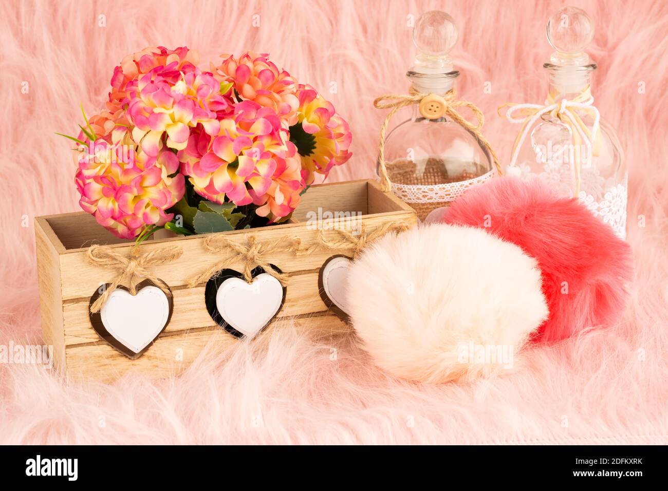 Beige Holzkiste, Blumen, Flaschen und flauschige Pompons auf Pelz Hintergrund. Stockfoto