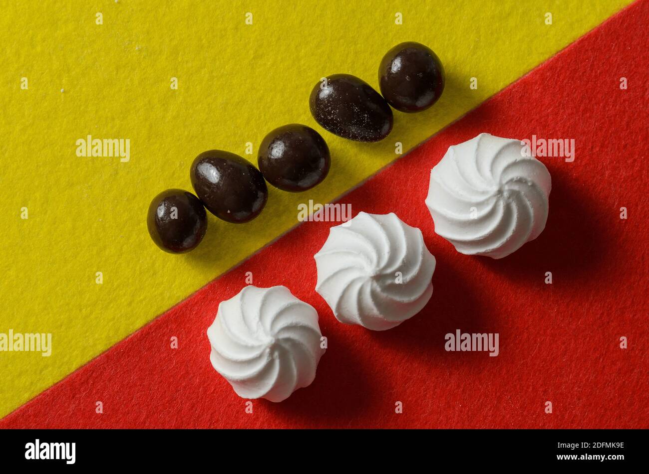 Weiße Baiser auf rotem Hintergrund mit runden SchokoladenBonbons auf gelbem Hintergrund. Selektiver Fokus. Stockfoto
