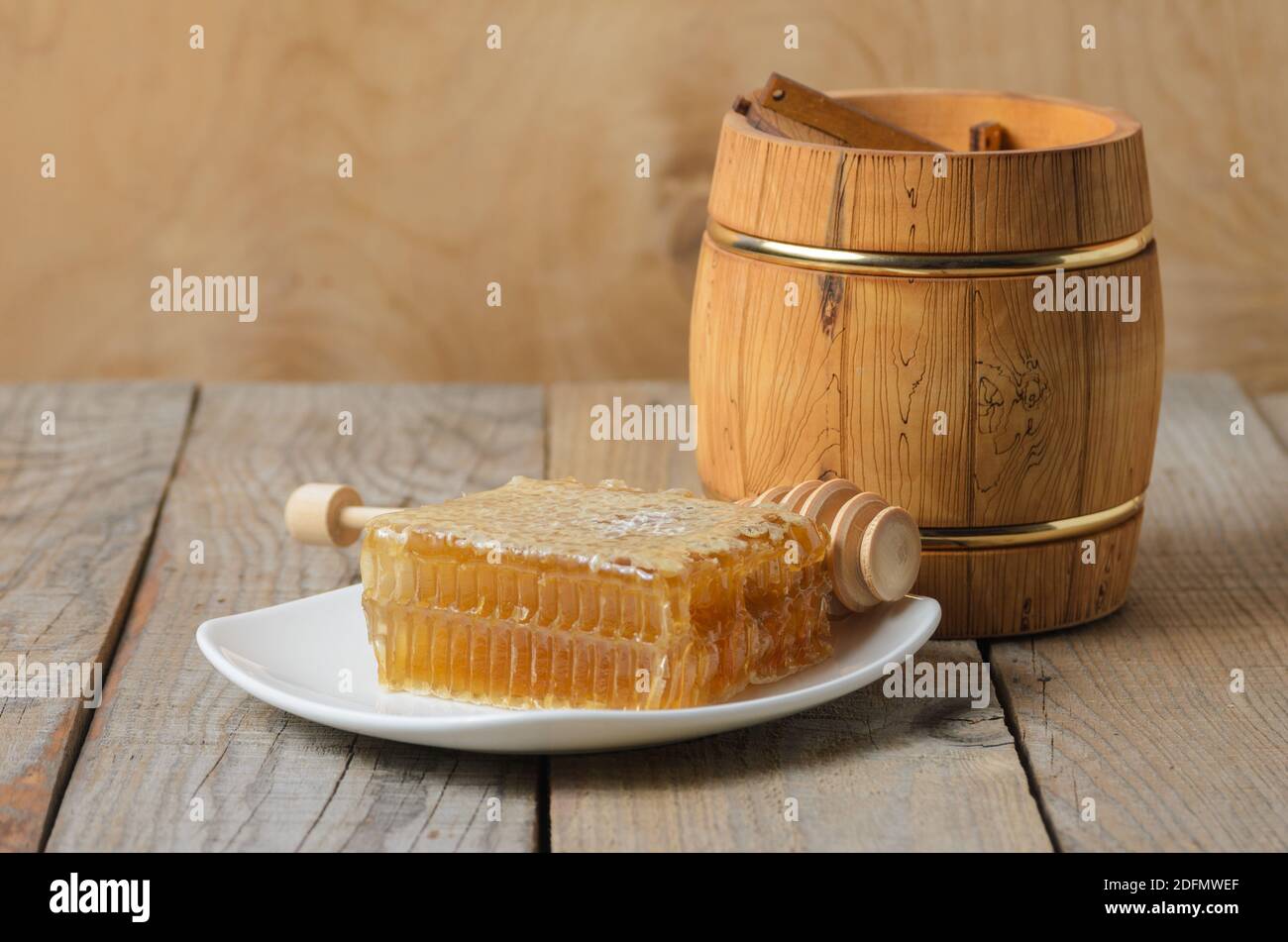 Honig in Honigwabe auf einem weißen Teller mit einem hölzernen Glas und Löffel auf einem rauen hölzernen Hintergrund. Selektiver Fokus. Stockfoto