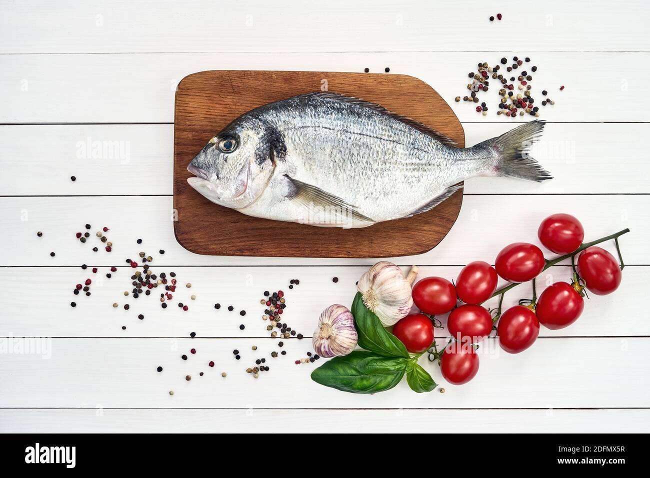 Frischer dorado-Fisch auf einem Holzschneidebrett mit Knoblauch, Tomaten, Basilikum und Pfefferkörnern. Draufsicht, Kopierbereich Stockfoto