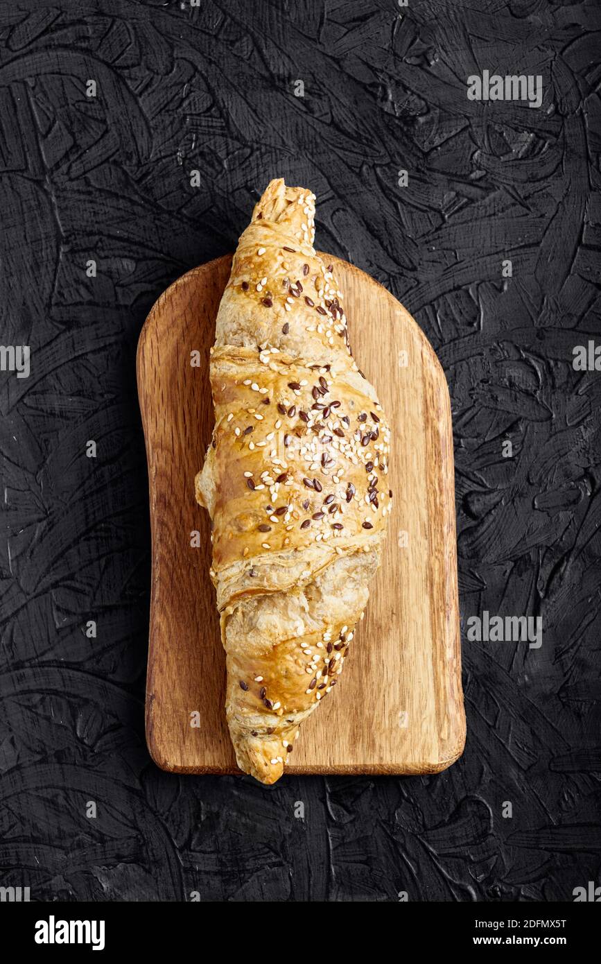 Frisches Croissant, Holzbrettschnitt, schwarzer Hintergrund. Draufsicht, Kopierbereich Stockfoto