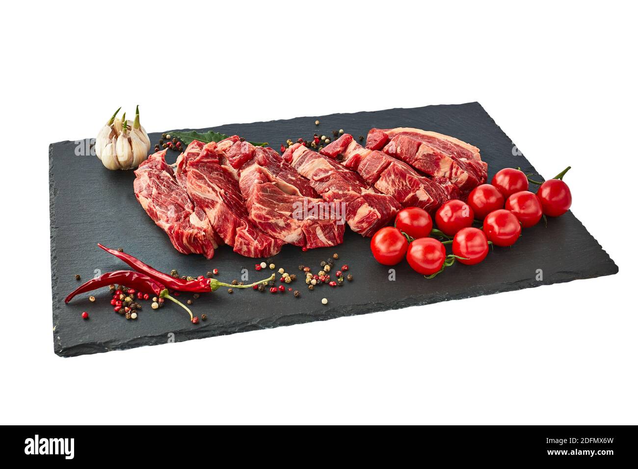 Frische rohe Rindersteaks mit Pfeffer und Tomaten auf einem schwarzen Schieferbrett. Isoliert über Weiß Stockfoto