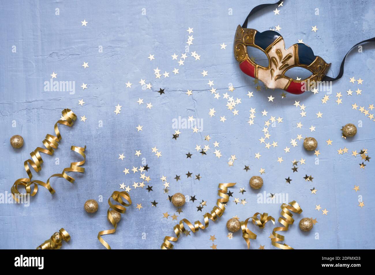 Venezianische Karnevalsmaske, Konfetti-Sterne und Party-Streamer auf blauem Hintergrund. Flaches Lay von Weihnachten, Jubiläum, Karneval, Neujahrsfeier con Stockfoto