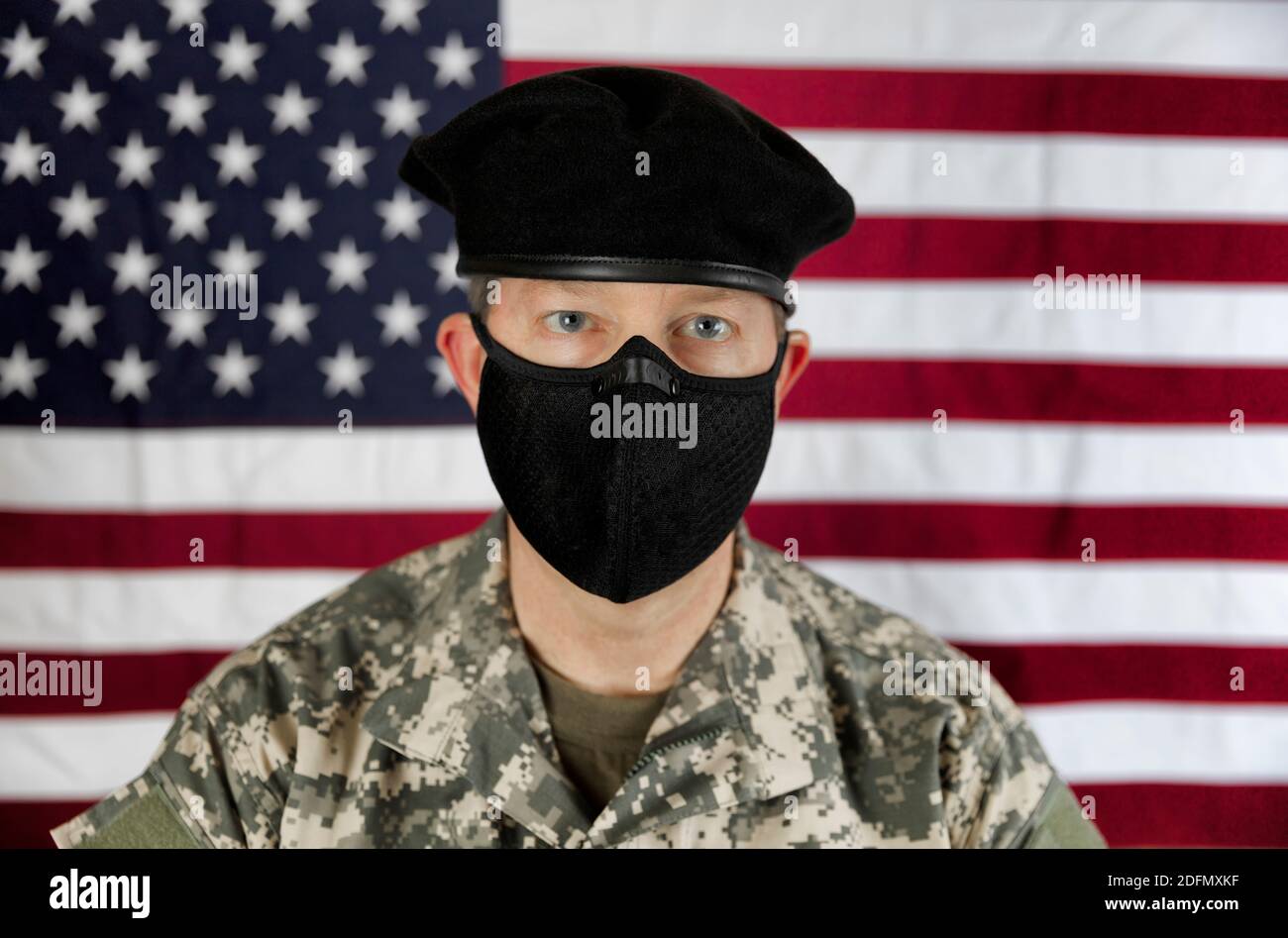 Männlicher US-Soldat mit Gesichtsmast zum Schutz vor einer Coronavirus-Pandemie. Fokus auf der Vorderseite der Maske mit USA Flagge im Hintergrund. Stockfoto