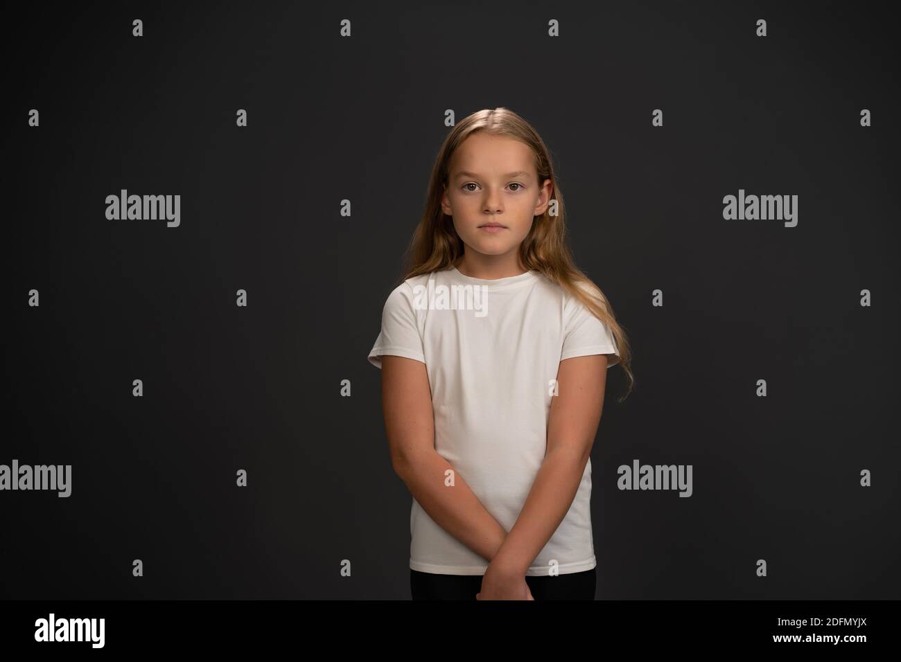 Kleines Mädchen steht und schaut fragwürdig oder frustriert auf die Kamera Tragen weißes T-Shirt isoliert auf dunkelgrauem oder schwarzem Hintergrund Stockfoto