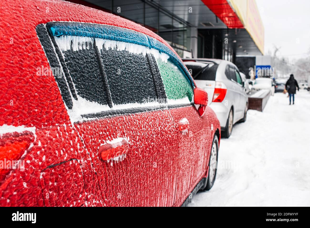 Rotes Auto bedeckt mit Eis und Eiszapfen nach kaltem Regen. Eissturmzyklon. Stadt im Winter. Schneebedecktes Wetter. Frostige Szenen im Winter. Stockfoto