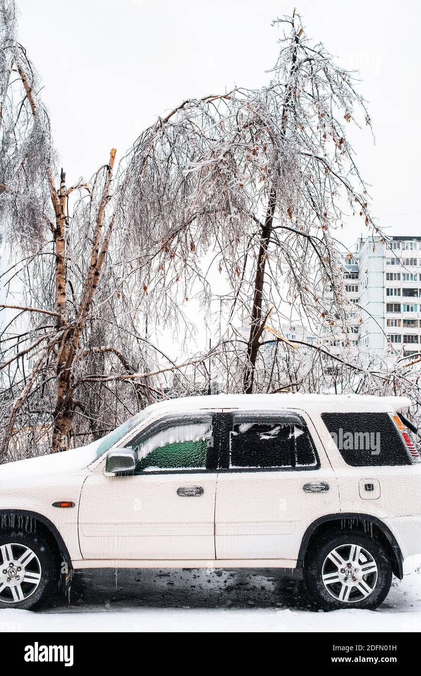 Weißes Auto bedeckt mit Eis und Schnee nach eisigen Regen. Eissturmzyklon. Stadt im Winter. Frostiges Wetter. Winterverschneite Szenen. Stockfoto
