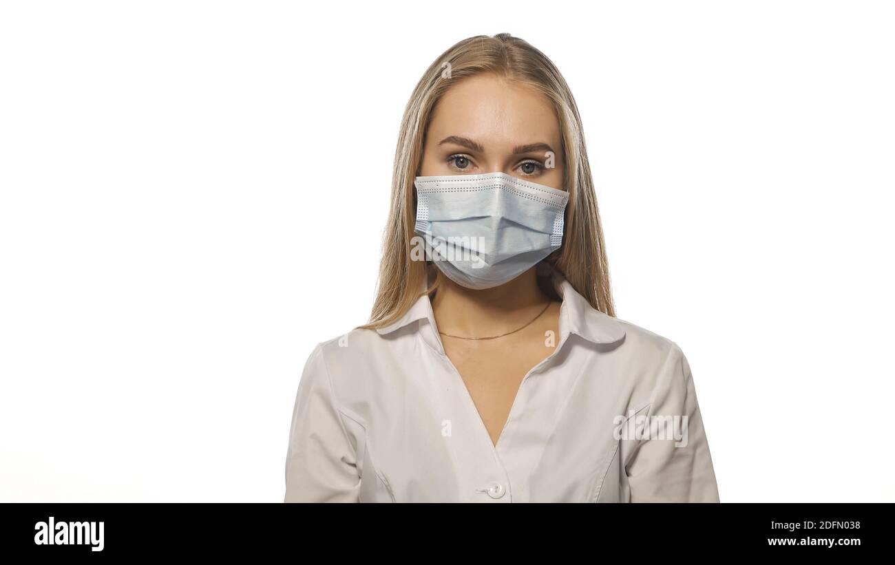 Krankenschwester in einer medizinischen Maske und weißen Uniform mit blondem lockeren Haar Blick auf die Kamera. Isoliert auf weißem Hintergrund Stockfoto