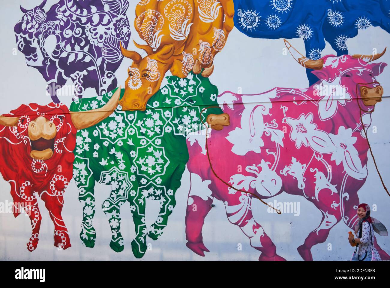 Eine indonesische Touristin verschwindet fast in einem bunten Wandbild von Büffeln in der Nähe von Buffalo Road, Little India, Singapur Stockfoto